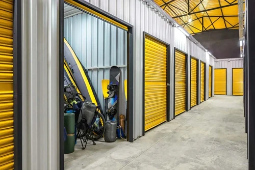 A photo of a storage unit with a snowboard, raft, lawn chair, and other outdoor gear stored in it.